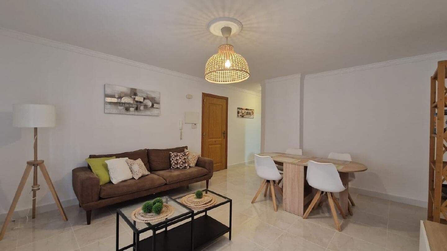 Salón-comedor reformado con sofá, mesa de comedor y lámpara de mimbre en un piso bajo de Las Lagunas de Mijas.